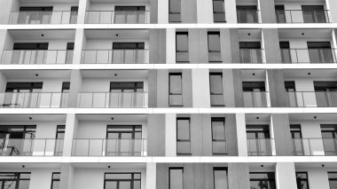 Pencereleri ve balkonları olan bir binanın ön cephesi. Birçok dairesi olan modern bir ev. Siyah ve beyaz.
