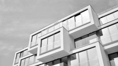 Pencereleri ve balkonları olan bir binanın ön cephesi. Birçok dairesi olan modern bir ev. Siyah ve beyaz.