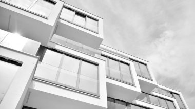 Pencereleri ve balkonları olan bir binanın ön cephesi. Birçok dairesi olan modern bir ev. Siyah ve beyaz.