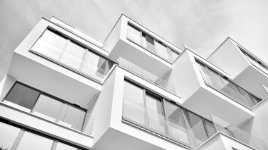 Pencereleri ve balkonları olan bir binanın ön cephesi. Birçok dairesi olan modern bir ev. Siyah ve beyaz.