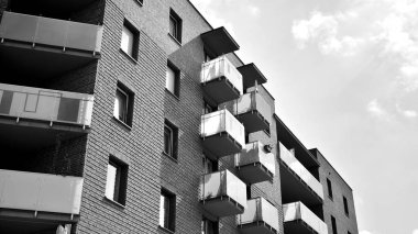 Pencereleri ve balkonları olan bir binanın ön cephesi. Birçok dairesi olan modern bir ev. Siyah ve beyaz.