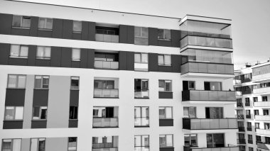 Pencereleri ve balkonları olan bir binanın ön cephesi. Birçok dairesi olan modern bir ev. Siyah ve beyaz.