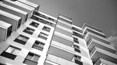 Pencereleri ve balkonları olan bir binanın ön cephesi. Birçok dairesi olan modern bir ev. Siyah ve beyaz.