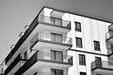 Pencereleri ve balkonları olan bir binanın ön cephesi. Birçok dairesi olan modern bir ev. Siyah ve beyaz.