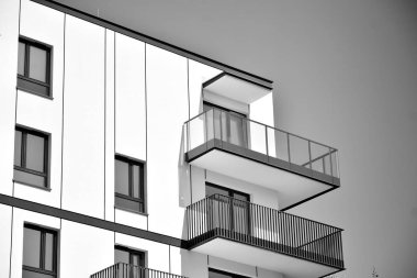 Pencereleri ve balkonları olan bir binanın ön cephesi. Birçok dairesi olan modern bir ev. Siyah ve beyaz.