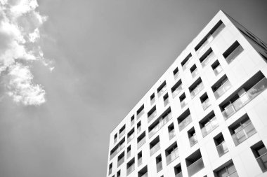 Pencereleri ve balkonları olan bir binanın ön cephesi. Birçok dairesi olan modern bir ev. Siyah ve beyaz.