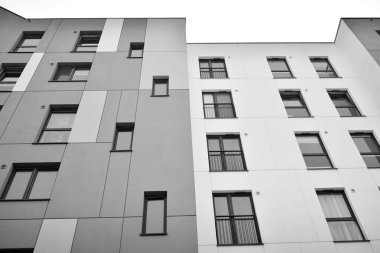 Pencereleri ve balkonları olan bir binanın ön cephesi. Birçok dairesi olan modern bir ev. Siyah ve beyaz.