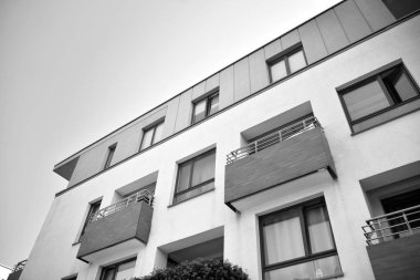Pencereleri ve balkonları olan bir binanın ön cephesi. Birçok dairesi olan modern bir ev. Siyah ve beyaz.