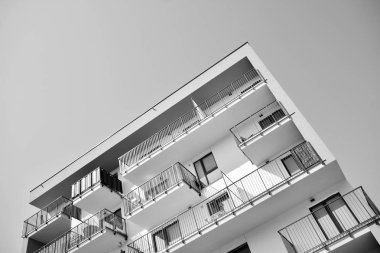 Pencereleri ve balkonları olan bir binanın ön cephesi. Birçok dairesi olan modern bir ev. Siyah ve beyaz.