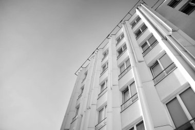 Pencereleri ve balkonları olan bir binanın ön cephesi. Birçok dairesi olan modern bir ev. Siyah ve beyaz.