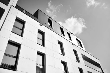 Pencereleri ve balkonları olan bir binanın ön cephesi. Birçok dairesi olan modern bir ev. Siyah ve beyaz.