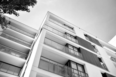 Pencereleri ve balkonları olan bir binanın ön cephesi. Birçok dairesi olan modern bir ev. Siyah ve beyaz.