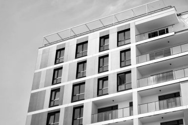 Pencereleri ve balkonları olan bir binanın ön cephesi. Birçok dairesi olan modern bir ev. Siyah ve beyaz.