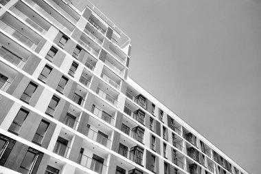 Pencereleri ve balkonları olan bir binanın ön cephesi. Birçok dairesi olan modern bir ev. Siyah ve beyaz.