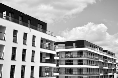 Pencereleri ve balkonları olan bir binanın ön cephesi. Birçok dairesi olan modern bir ev. Siyah ve beyaz.