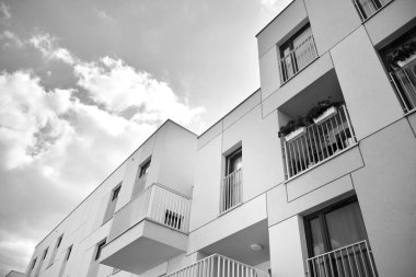 Pencereleri ve balkonları olan bir binanın ön cephesi. Birçok dairesi olan modern bir ev. Siyah ve beyaz.