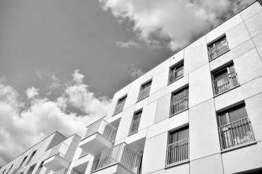 Pencereleri ve balkonları olan bir binanın ön cephesi. Birçok dairesi olan modern bir ev. Siyah ve beyaz.