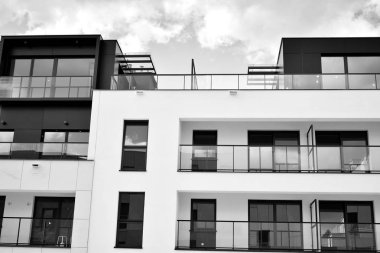 Pencereleri ve balkonları olan bir binanın ön cephesi. Birçok dairesi olan modern bir ev. Siyah ve beyaz.