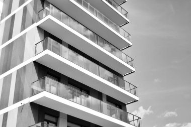 Pencereleri ve balkonları olan bir binanın ön cephesi. Birçok dairesi olan modern bir ev. Siyah ve beyaz.
