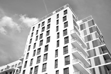 Pencereleri ve balkonları olan bir binanın ön cephesi. Birçok dairesi olan modern bir ev. Siyah ve beyaz.