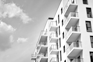 Pencereleri ve balkonları olan bir binanın ön cephesi. Birçok dairesi olan modern bir ev. Siyah ve beyaz.