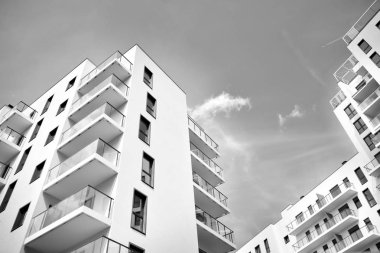 Pencereleri ve balkonları olan bir binanın ön cephesi. Birçok dairesi olan modern bir ev. Siyah ve beyaz.