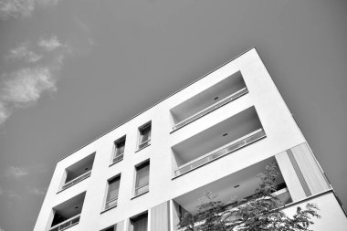 Pencereleri ve balkonları olan bir binanın ön cephesi. Birçok dairesi olan modern bir ev. Siyah ve beyaz.