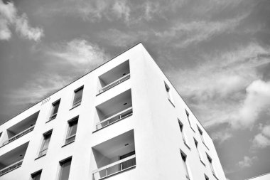 Pencereleri ve balkonları olan bir binanın ön cephesi. Birçok dairesi olan modern bir ev. Siyah ve beyaz.