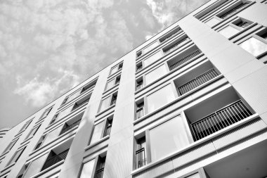 Pencereleri ve balkonları olan bir binanın ön cephesi. Birçok dairesi olan modern bir ev. Siyah ve beyaz.