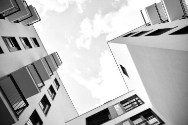 Pencereleri ve balkonları olan bir binanın ön cephesi. Birçok dairesi olan modern bir ev. Siyah ve beyaz.