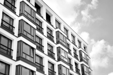 Pencereleri ve balkonları olan bir binanın ön cephesi. Birçok dairesi olan modern bir ev. Siyah ve beyaz.