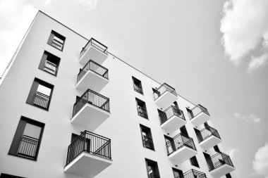 Pencereleri ve balkonları olan bir binanın ön cephesi. Birçok dairesi olan modern bir ev. Siyah ve beyaz.