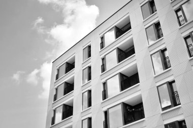 Pencereleri ve balkonları olan bir binanın ön cephesi. Birçok dairesi olan modern bir ev. Siyah ve beyaz.