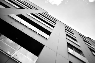 Pencereleri ve balkonları olan bir binanın ön cephesi. Birçok dairesi olan modern bir ev. Siyah ve beyaz.