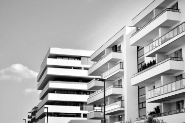 Pencereleri ve balkonları olan bir binanın ön cephesi. Birçok dairesi olan modern bir ev. Siyah ve beyaz.