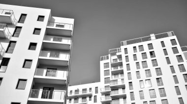 Pencereleri ve balkonları olan bir binanın ön cephesi. Birçok dairesi olan modern bir ev. Siyah ve beyaz.