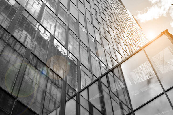 Facade texture of a glass mirrored office building. Fragment of the facade. Bottom view of modern skyscrapers in business district in evening light at sunset with lens flare filter effect. Black and white.