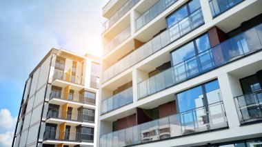 Mavi gökyüzü olan güneşli bir günde modern apartman binaları. Modern bir apartmanın ön cephesi. Güneş ışığıyla cam yüzey.