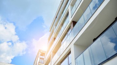 Mavi gökyüzü olan güneşli bir günde modern apartman binaları. Modern bir apartmanın ön cephesi. Güneş ışığıyla cam yüzey.