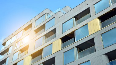 Mavi gökyüzü olan güneşli bir günde modern apartman binaları. Modern bir apartmanın ön cephesi. Güneş ışığıyla cam yüzey.