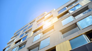 Mavi gökyüzü olan güneşli bir günde modern apartman binaları. Modern bir apartmanın ön cephesi. Güneş ışığıyla cam yüzey.