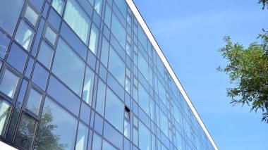 Mavi gökyüzünün altındaki tonlu cam ve çelik yapılardan yapılmış mavi perde duvarı. Bir binanın parçası..