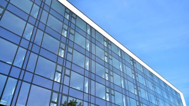 Mavi gökyüzünün altındaki tonlu cam ve çelik yapılardan yapılmış mavi perde duvarı. Bir binanın parçası..