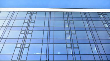 Mavi gökyüzünün altındaki tonlu cam ve çelik yapılardan yapılmış mavi perde duvarı. Bir binanın parçası..