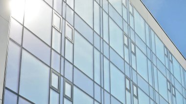 Mavi gökyüzünün altındaki tonlu cam ve çelik yapılardan yapılmış mavi perde duvarı. Bir binanın parçası..