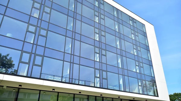 Blue curtain wall made of toned glass and steel constructions under blue sky. A fragment of a building.