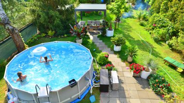 Garden of a suburban house in summer in which you can see a removable swimming pool, pergola in a place with a lot of vegetation.