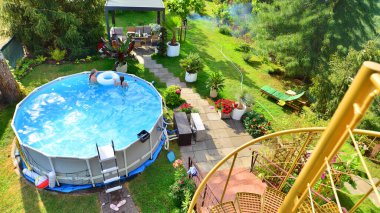 Garden of a suburban house in summer in which you can see a removable swimming pool, pergola in a place with a lot of vegetation.