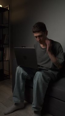 Genç serbest çalışan, kötü duruş nedeniyle boyun ağrısı çekiyor. Kanepede kambur oturuyor ve otantik ev ortamında dizüstü bilgisayarla çalışıyor. Yerleşik işlerin, aygıtların rahatsızlığının ve ev ofis yaşam tarzının vurgulanması.