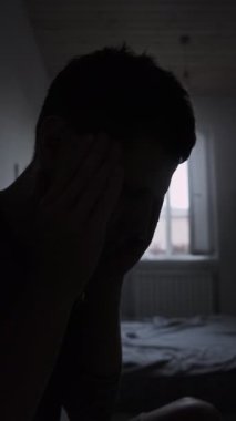 Erkek silueti baş ağrısı için tapınaklara masaj yapıyor. Soğuk ışık, otantik yaşam tarzı, dikey video.